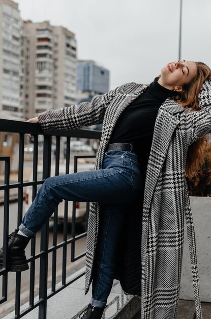 Uma mulher de casaco e jeans se inclina sobre uma grade