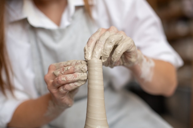 Uma mulher de ceramista trabalha com argila na roda de oleiro. A criação do vaso. Oficina de cerâmica. Fechar-se