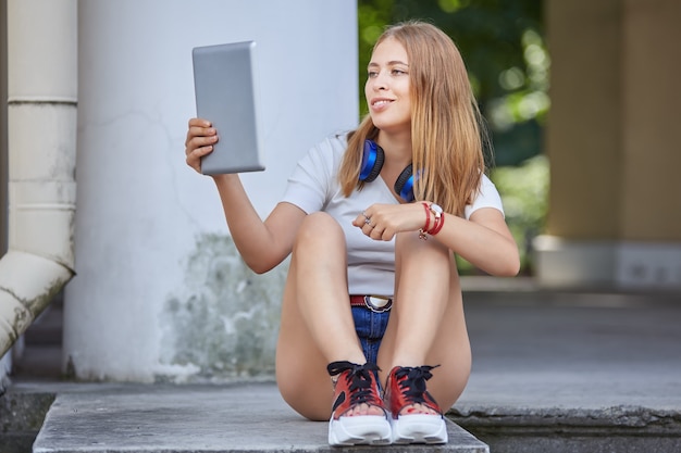 Uma mulher de cerca de 20 anos está usando um tablet pc para bater um papo com amigos enquanto está sentada na escada.