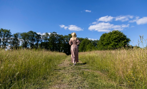 Uma mulher de chapéu atravessa o campo na grama cortada