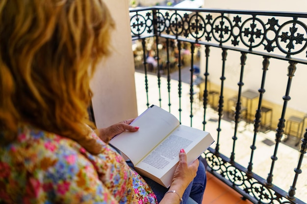 Foto uma mulher de costas lendo um livro no terraço de suas casas em um dia ensolarado e quente