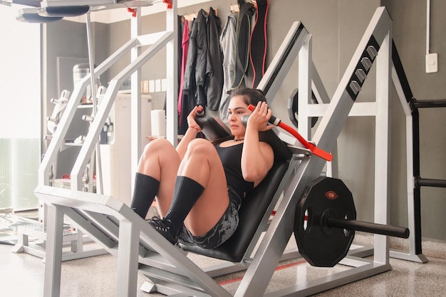 Uma mulher de fitness a fazer um agachamento profundo na máquina de hack no ginásio.