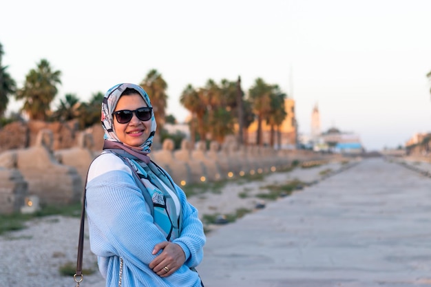 Uma mulher de jaqueta azul e óculos de sol fica em frente ao antigo templo egípcio em Luxor
