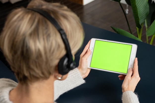 Uma mulher de meia idade com um fone de ouvido está vendo conteúdo usando um tablet em uma tela verde, ligando para ela