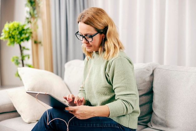 Uma mulher de meia-idade relaxando em casa e usando tablet para música ou videochamada