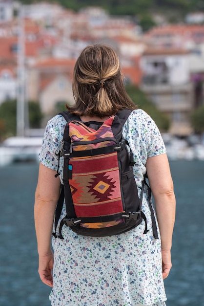 Uma mulher de meia-idade viaja pelo mundo com uma mochila nas costas com um ornamento olhando para o mar