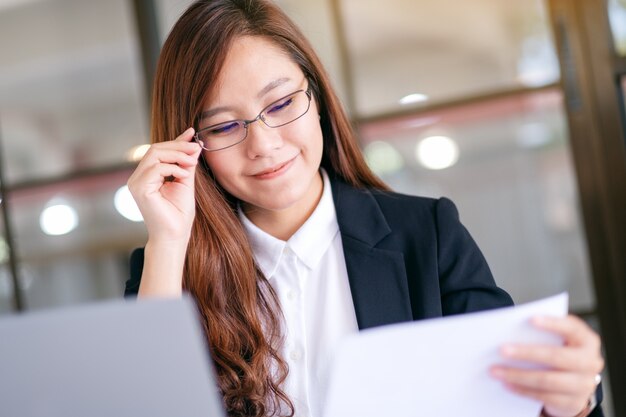 Uma mulher de negócios asiática usando e trabalhando em um laptop e a papelada no escritório