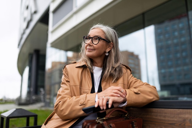 Uma mulher de negócios em óculos senta-se em um banco no contexto de um centro de negócios