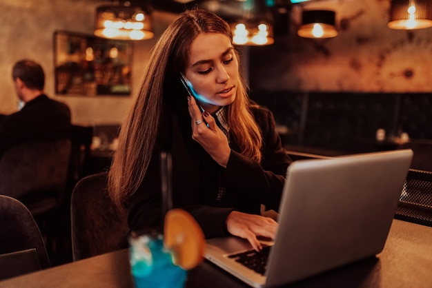 Uma mulher de negócios em óculos sentado em um café usando um laptop e um smartphone para reunião online Foco seletivo