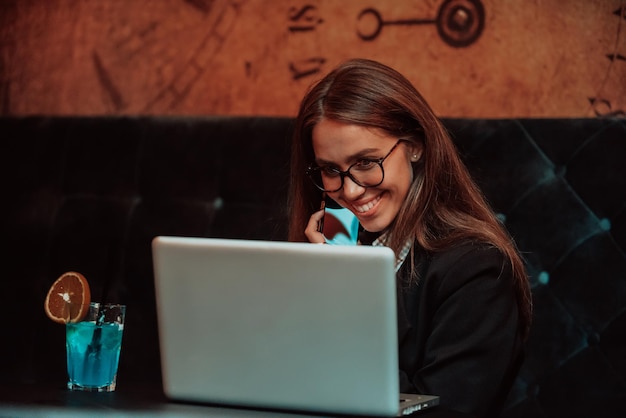 Uma mulher de negócios em óculos sentado em um café usando um laptop e um smartphone para reunião online Foco seletivo