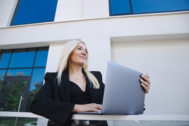 Uma mulher de negócios em um terno elegante está trabalhando em um laptop na rua