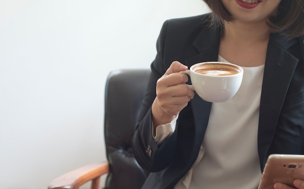 Uma mulher de negócios está segurando uma xícara de café branca durante o trabalho no escritório