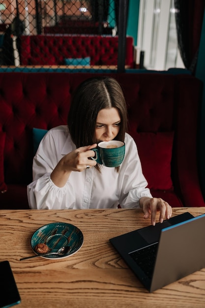 Uma mulher de negócios está sentada à mesa de um café com uma xícara de café e trabalhando em um laptop