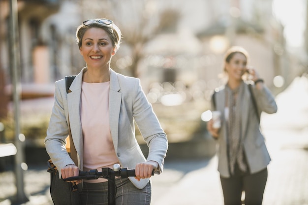 Uma mulher de negócios madura vai trabalhar com uma scooter elétrica.