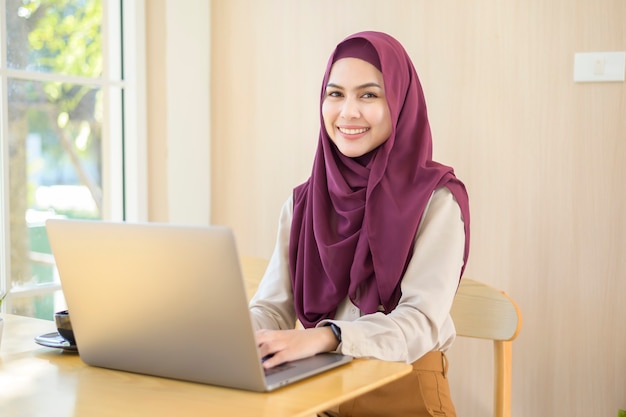 Uma mulher de negócios muçulmana usando hijab e trabalhando com seu laptop em uma cafeteria