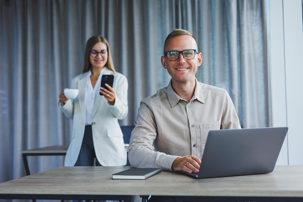 Uma mulher de negócios na frente de um colega do sexo masculino que trabalha em um laptop Cooperação empresarial e trabalho em equipe Trabalhadores de escritório europeus à mesa no escritório Pessoas modernas de sucesso