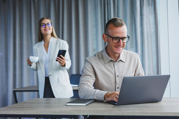 Uma mulher de negócios na frente de um colega do sexo masculino que trabalha em um laptop cooperação empresarial e trabalho em equipe trabalhadores de escritório europeus à mesa no escritório pessoas modernas de sucesso