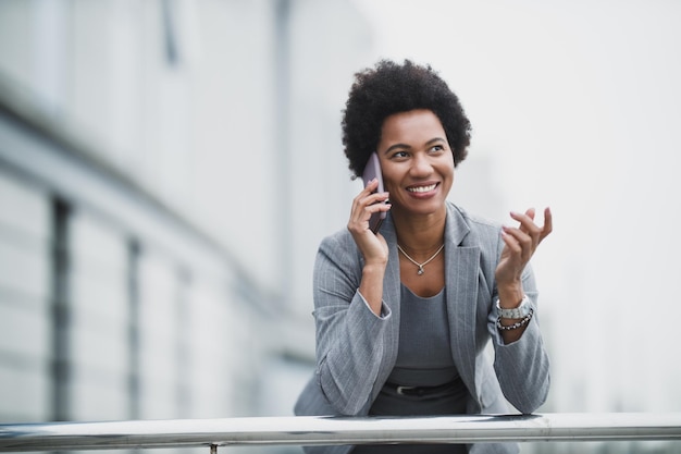 Uma mulher de negócios negra bem-sucedida usando telefone inteligente em frente a um prédio corporativo.