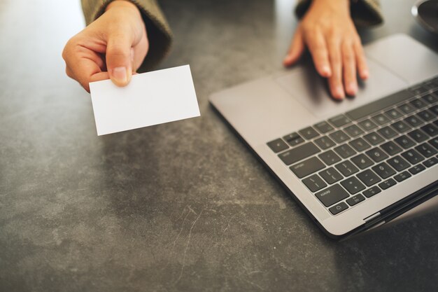 Uma mulher de negócios segurando e dando cartões de visita em branco enquanto usa o laptop no escritório