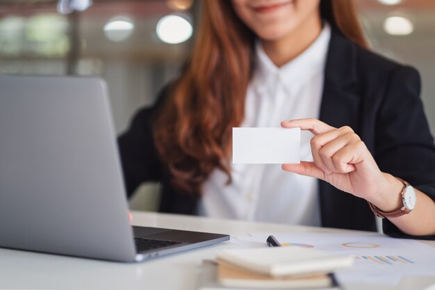 Uma mulher de negócios segurando e mostrando cartões de visita em branco enquanto usa um laptop no escritório