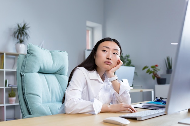 Uma mulher de negócios triste trabalha em um escritório moderno uma mulher asiática pensa nos resultados do trabalho