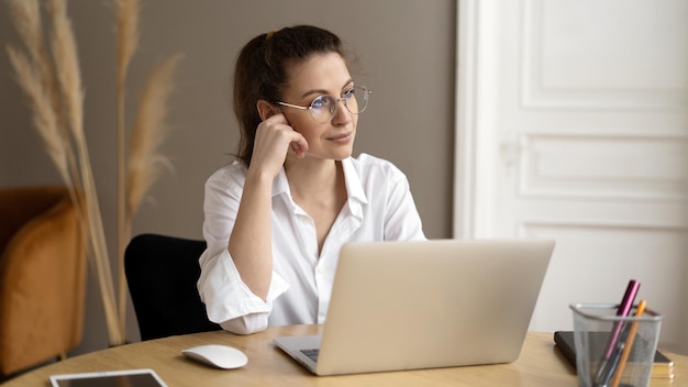 Uma mulher de óculos é uma freelancer trabalhando em um escritório usando um laptop