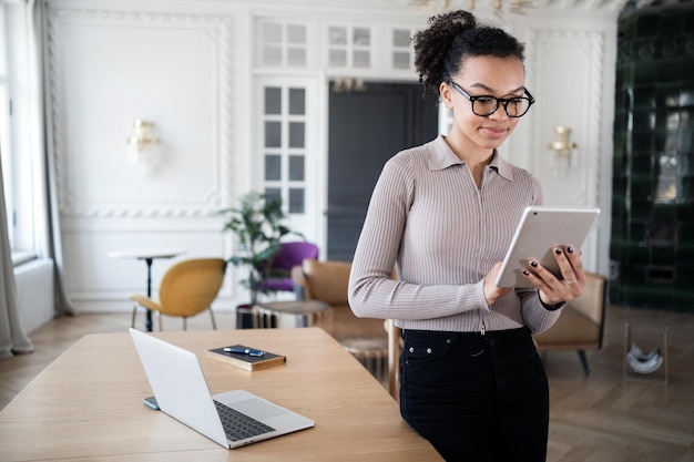 Uma mulher de óculos trabalha no local de trabalho de uma empresa financeira no escritório usa um laptop e a Internet