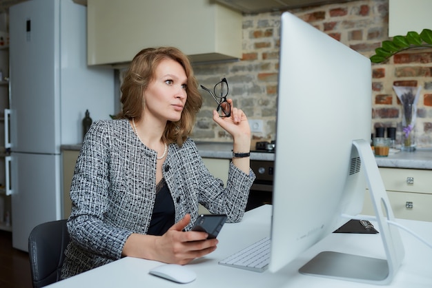 Uma mulher de óculos trabalha remotamente em um computador desktop em seu estúdio. Uma senhora usa um telefone durante uma videoconferência em casa. Uma professora ouvindo as respostas dos alunos em uma aula on-line.