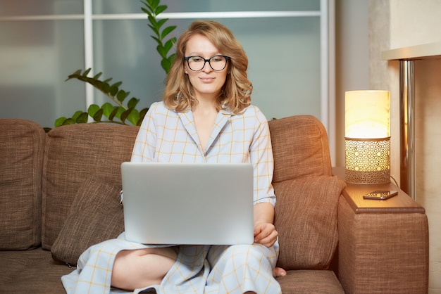 Uma mulher de óculos trabalha remotamente em um laptop em seu apartamento. Uma garota durante uma videoconferência com seus colegas em casa.