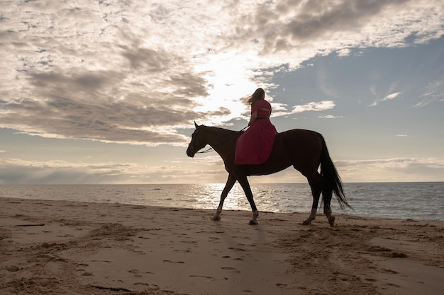 Uma mulher de rosa montando um cavalo preto na praia