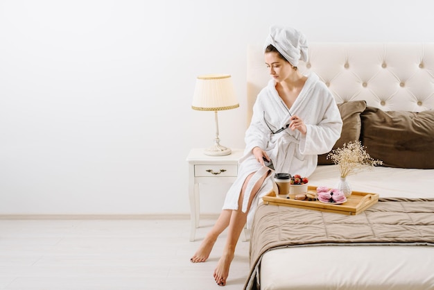 Uma mulher de roupão com toalha na cabeça usando smathphone na cama em casa