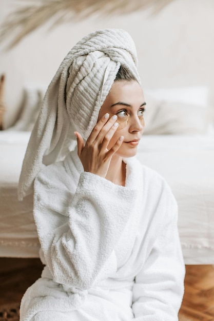 uma mulher de roupão de banho está de pé na frente de uma cama com uma toalha enrolada em torno de sua cabeça
