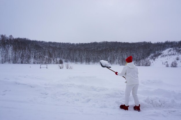 Uma mulher de terno branco limpa a neve no quintal