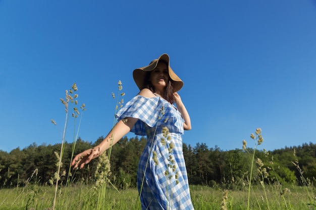 Uma mulher de vestido azul e chapéu de palha fica no campo e ri Vida sem conceito de alergia