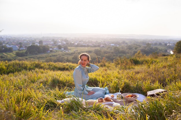 Uma mulher de vestido azul senta-se em um piquenique em um parque com vista panorâmica