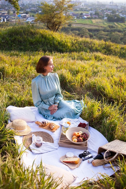 Uma mulher de vestido azul senta-se em um piquenique em um parque com vista panorâmica