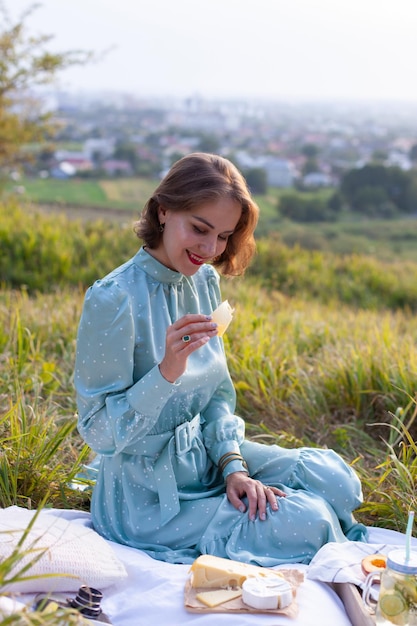 Uma mulher de vestido azul senta-se em um piquenique em um parque com vista panorâmica