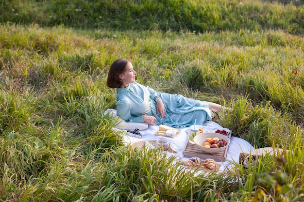 Uma mulher de vestido azul senta-se em um piquenique em um parque com vista panorâmica