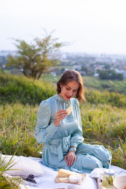 Uma mulher de vestido azul senta-se em um piquenique em um parque com vista panorâmica