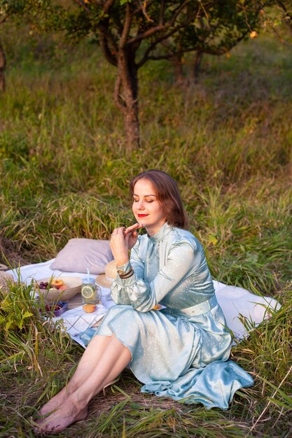 Uma mulher de vestido azul senta-se em um piquenique em um parque com vista panorâmica