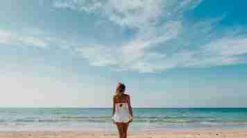 Foto uma mulher de vestido branco está na praia em frente ao oceano