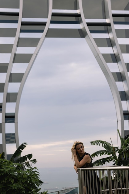 Uma mulher de vestido preto posa em frente a um prédio que tem um grande arco que diz 'eu te amo'