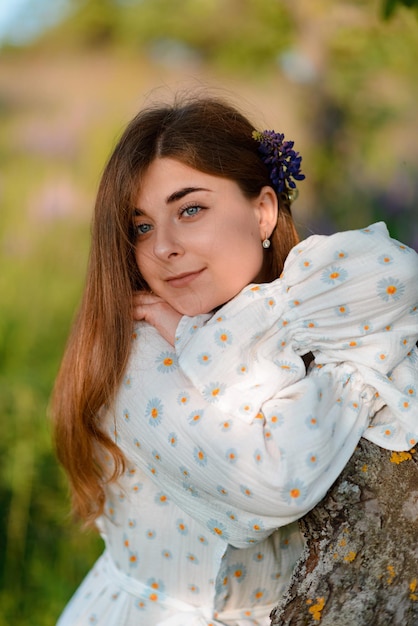 Foto uma mulher de vestido retro de pé junto a uma árvore e olhando para a câmera