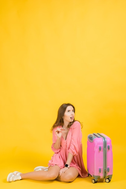 Uma mulher de vestido rosa tem nas mãos uma grande mala rosa viagem de bagagem