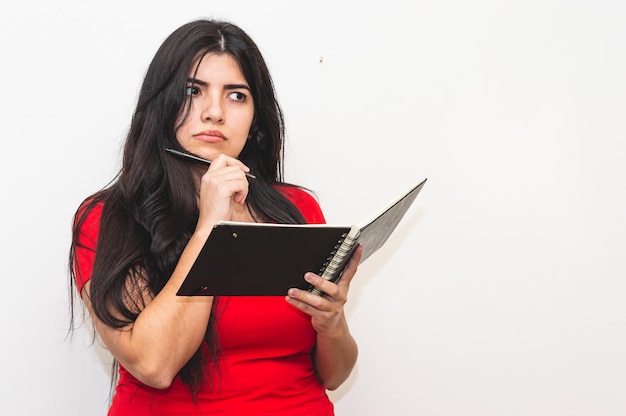 Uma mulher de vestido vermelho está segurando uma caneta e olhando para um caderno.