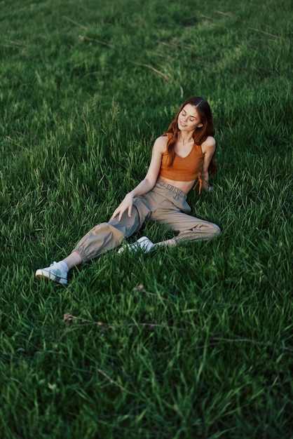Uma mulher deita-se na grama verde fresca da primavera em um parque e gosta de relaxar assistindo a luz do sol do pôr do sol Foto de alta qualidade