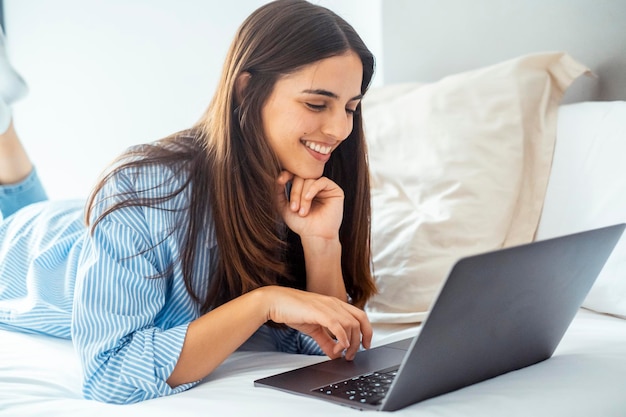 uma mulher deitada em uma cama com um laptop no colo