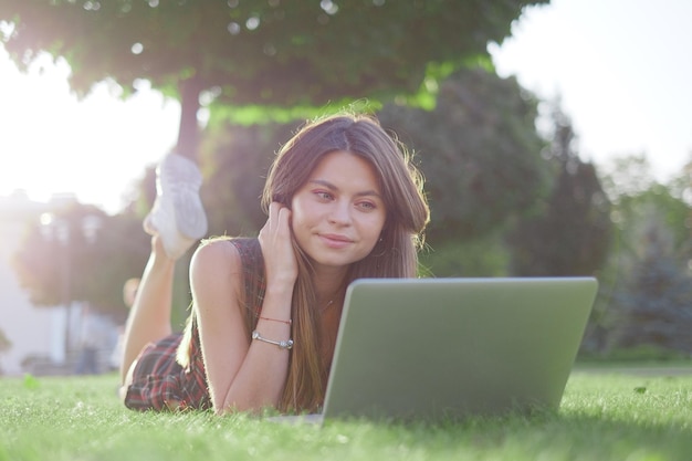 Uma mulher deitada na grama com um laptop na mão.