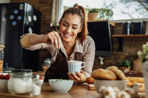 uma mulher derramando uma chávena de chá em uma cozinha