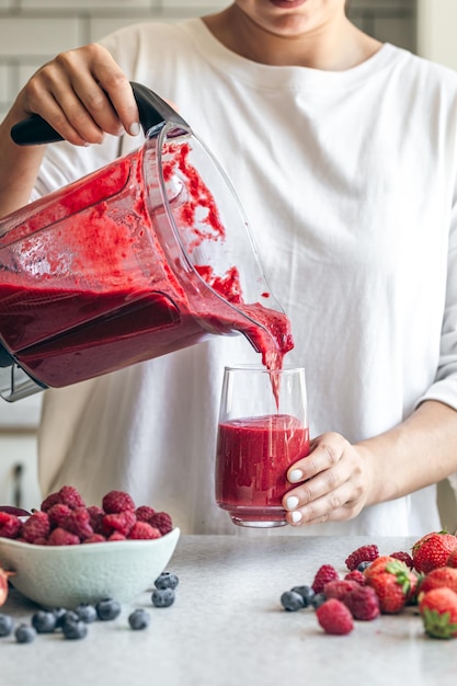 Uma mulher despeja um smoothie de bagas de um liquidificador em um copo